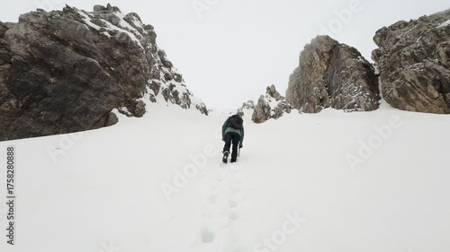 Mountaineer climbing a snowy couloir between steep rocky walls in winter conditions.
