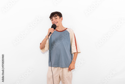 young casual dressed Generation Z influencer white male host model teenage boy with microphone for singing, presenting and interviewing for social media channel. plain background studio setting