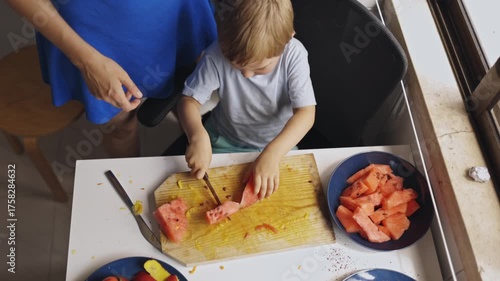 Mother teaching child to cut watermelon in kitchen