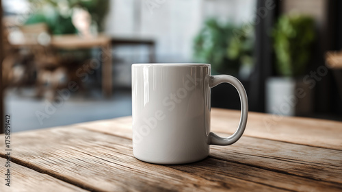 A blank white mug sits on a wooden table against a blurred background in a cafe