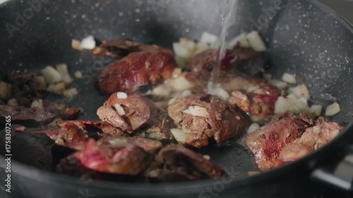 Cooking liver pieces in a frying pan with steam rising and kitchen appliances in the background