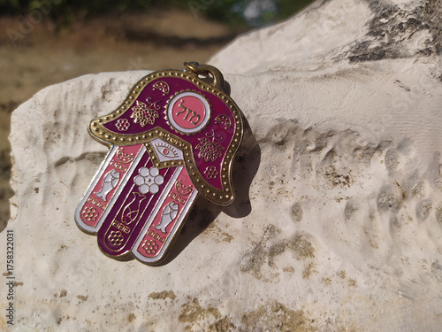 A close-up of the Hamsa hand amulet on a sunlit stone. A metal Jewish keychain, 