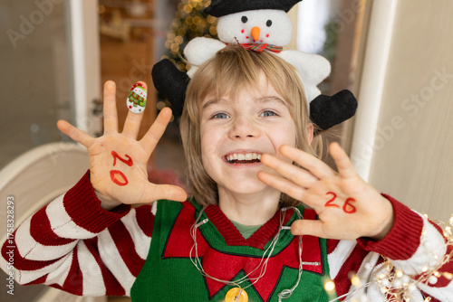 joyful, laughing child shows his palms with the numbers 2026 written on them. Home comfort and fun on Christmas Eve. Let's make a wish and look forward to pleasant changes in the new year