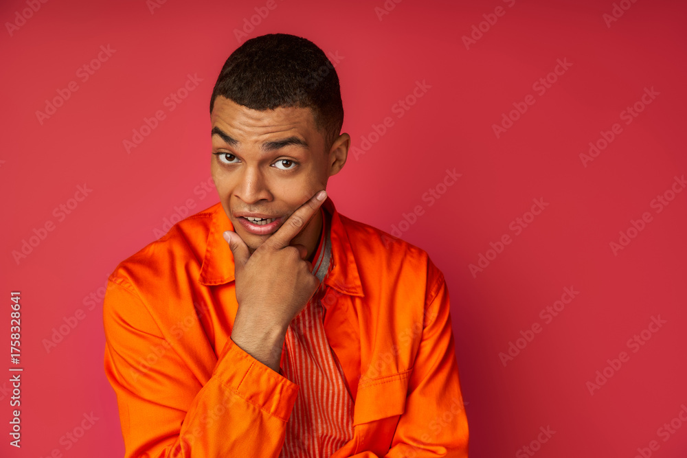 Obraz premium Young man expresses joy and confidence in vibrant orange attire against bright pink backdrop