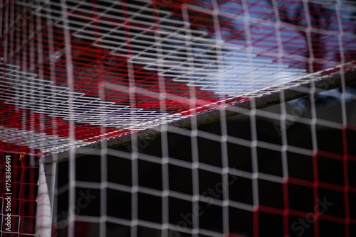 Red and white soccer goal net with repeating square mesh at the corner; minimalist sports texture and geometry.