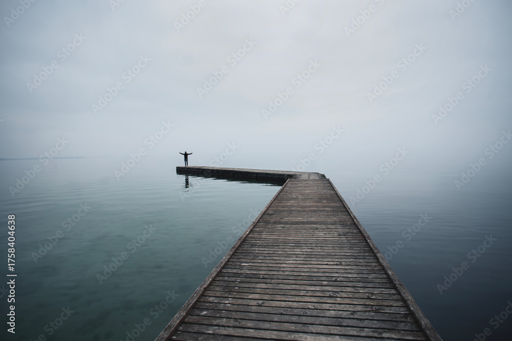 Obraz premium Man with arms raised against the light at the end of a pier on the sea in the evening light