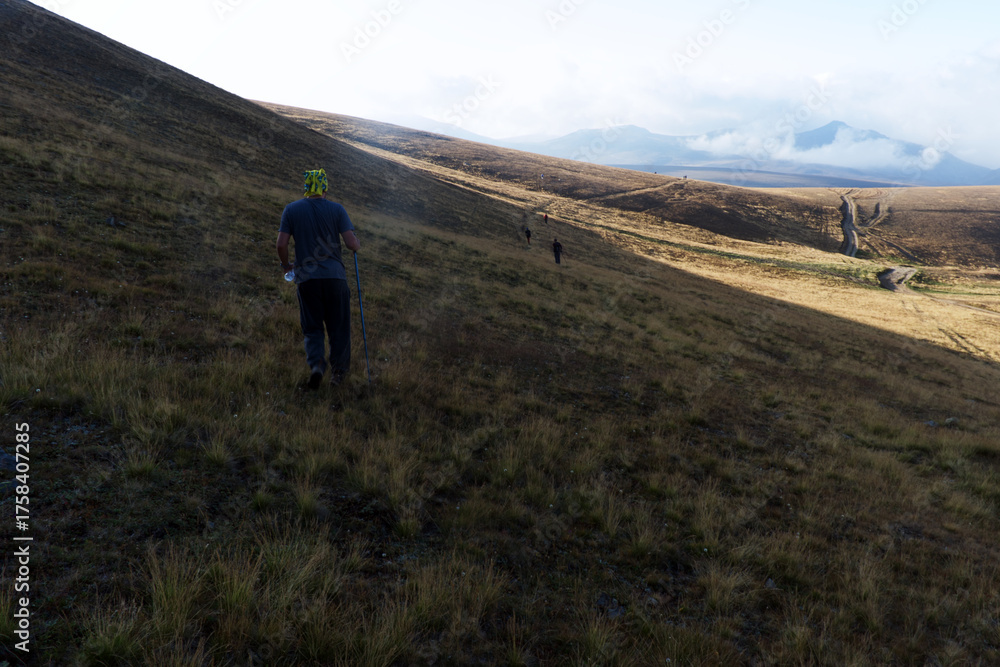 Obraz premium A group of hikers ascending a sunlit mountain slope in the early morning light. The warm tones of sunrise highlight endurance, teamwork, and exploration in nature.