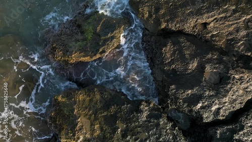 Aerial view of foamy sea waves breaking on the rocky coast, top view.