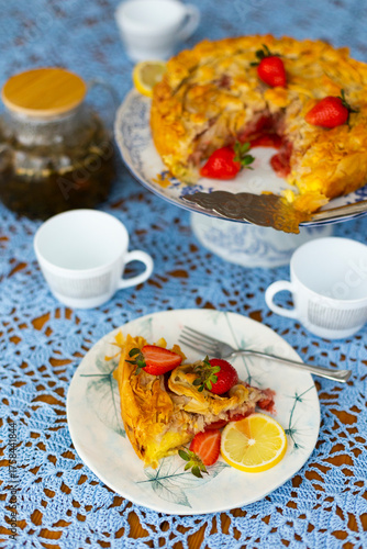 Piece of strawberry pie with lemon and fresh berries on lace light blue tablecloth