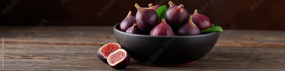 Fototapeta premium Fresh purple figs in black bowl on rustic wooden table with sliced fig