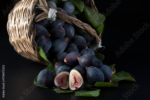 Fichi viola maturi in un cesto di vimini su sfondo nero