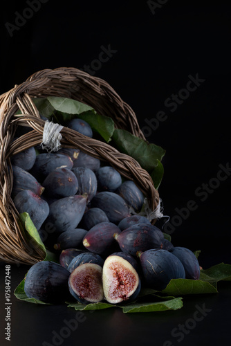Fichi freschi in un cestino su sfondo nero con foglie.