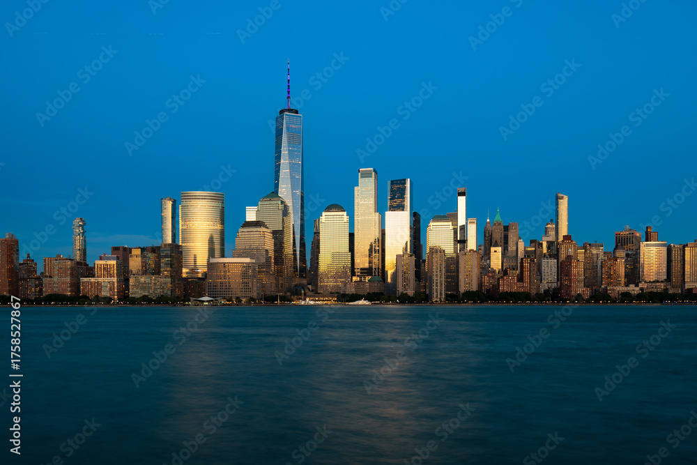 Fototapeta premium The illuminated New York City skyline of downtown Manhattan, with buildings glowing in the golden light of the evening.