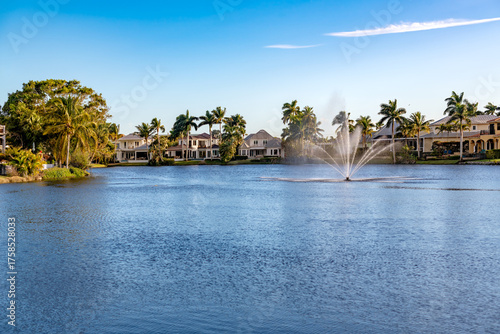 Fototapeta Naklejka Na Ścianę i Meble -  The serene residential area of Spring Lake in Naples, Florida, with large homes and tropical palm trees around a lake with a fountain.
