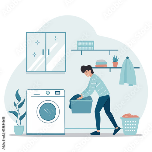 A young man is engaged in household chores, loading dirty clothes from a basket into the washing machine in a modern laundry room