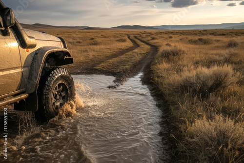 Off-road vehicle driving through muddy water on a dirt track in the steppe at sunset, adventure SUV splashing mud in golden light, symbolizing freedom, travel, and exploration in wild nature terrain.