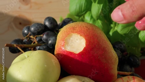Fruits lie on a surface. A hand picks up a pear, takes a bite, and places it back. Close-up shot.