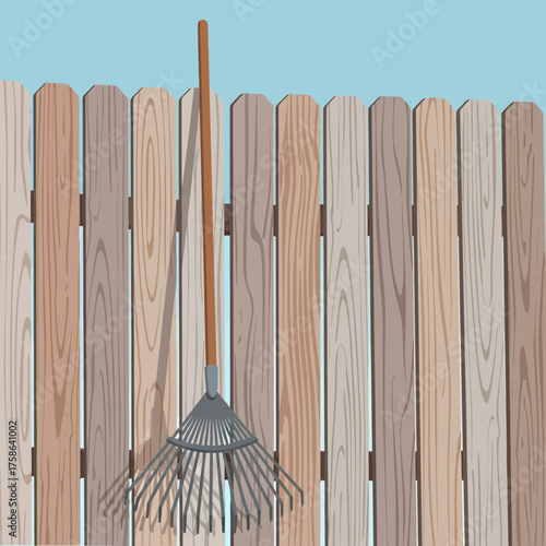 A rake leans against a wooden fence.