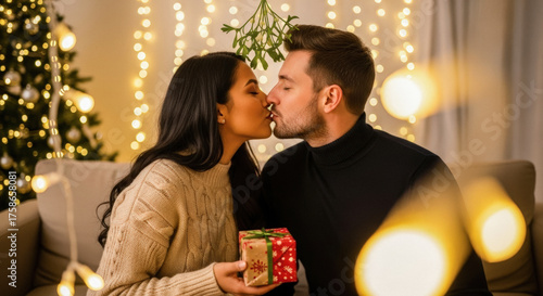 Romantic couple sharing a kiss under mistletoe with a gift, celebrating Christmas in a cozy, warm-lit living room.