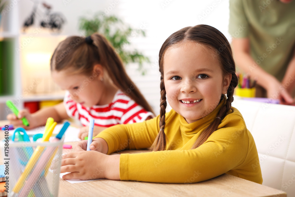 Fototapeta premium Smiling little girls at wooden desk during lesson in elementary school