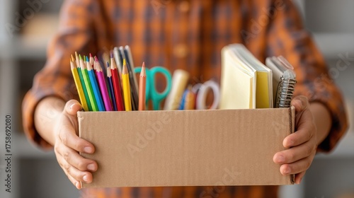 volunteer holds hands Cardboard donation with school stationery items. donate written on the box. Concept: donate of stationery. back to school. start of the school year. School supplies donation