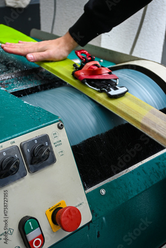 Person's hand guiding ski on automated waxing and grinding machine, preparing for winter sport season
