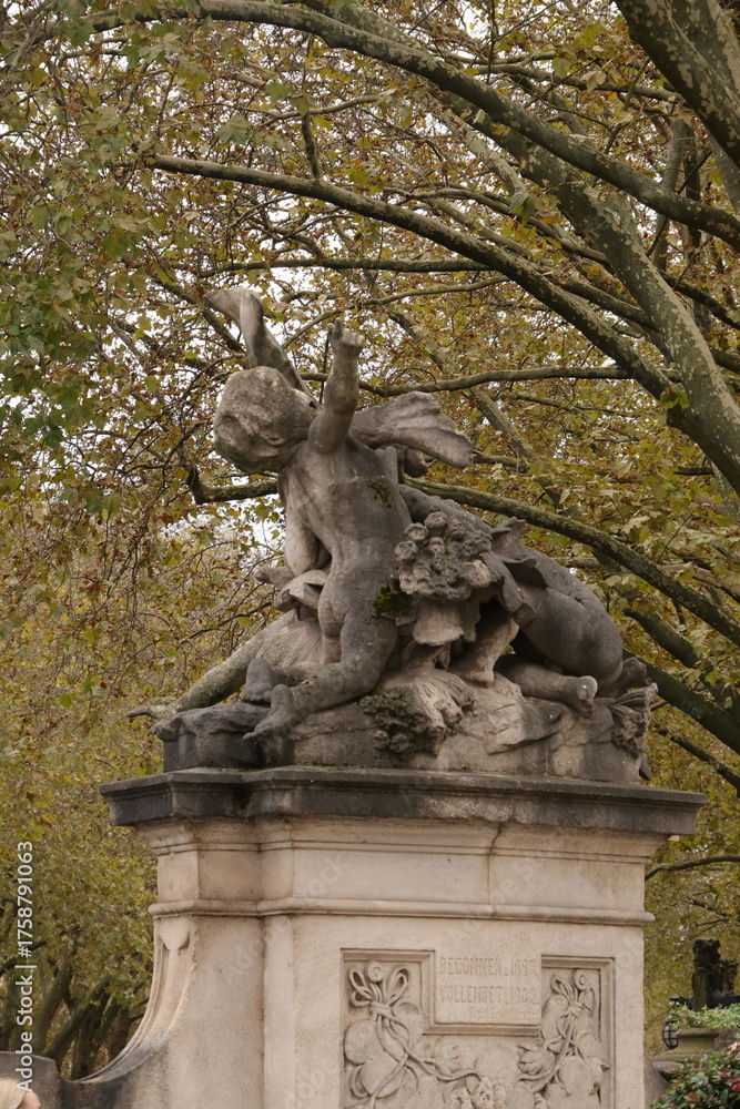 Fototapeta premium Historic Stone Statue Surrounded By Trees In A Düsseldorf Park Monument Scene At Dusk