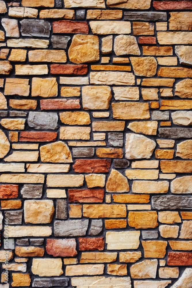 Fototapeta premium a rustic stone wall featuring an irregular, multicolored pattern of roughly rectangular and irregularly shaped stones in shades of beige, brown, gray, and red.