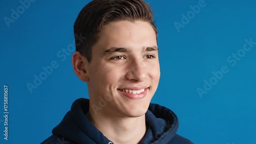 A smiling person with dark hair and brown eyes, wearing a dark blue hoodie, against a blue backdrop