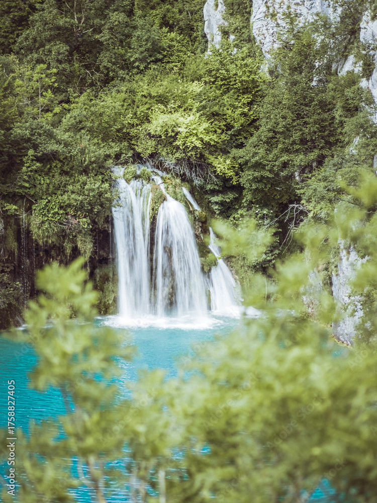 Fototapeta premium Beautiful view of a cascading waterfall flowing into a turquoise lake surrounded by lush green forest in Plitvice Lakes National Park, Croatia.
