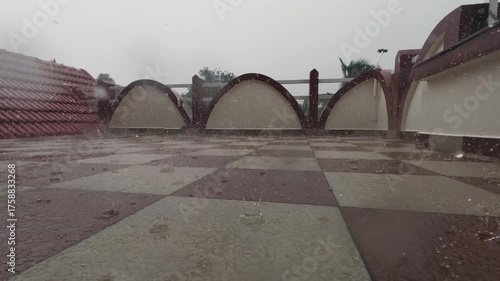 Rain falling on a tiled floor with arched wall barriers in the background. A peaceful monsoon moment capturing the wet textures and moody atmosphere of a rainy day