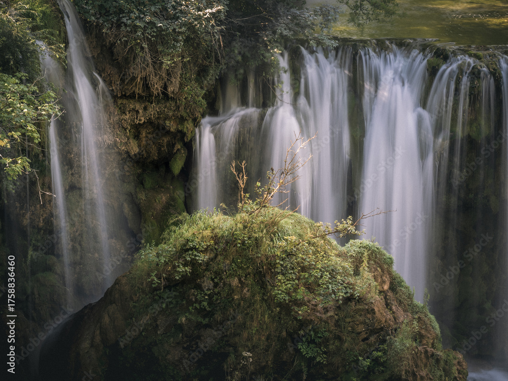 Obraz premium Close view of multiple waterfalls dropping over a mossy cliff around a rocky outcrop, with lush vegetation in Rastoke, Croatia.
