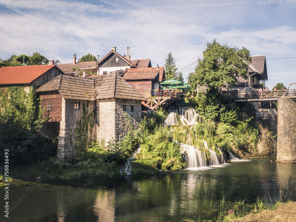 Obraz premium Traditional watermill houses beside cascading waterfalls in the village of Rastoke, Croatia, where historic architecture meets lush greenery.