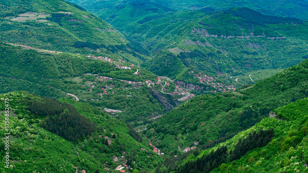 Fototapeta premium An aerial perspective of a mountain valley filled with green forests and scattered villages surrounded by hills, roads, and nature.