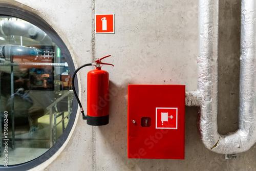 Fire safety equipment including a red extinguisher and hose cabinet on a concrete wall in an industrial facility. Concept of emergency preparedness and workplace safety.