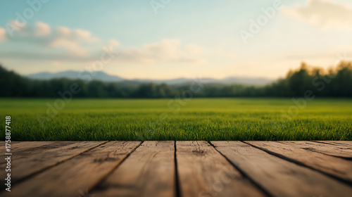 Fototapeta Naklejka Na Ścianę i Meble -  Captivating scenery unfolds from a weathered wood deck, inviting calm. Lush green meadow meets a horizon blurred by trees, all under a serene sky glow. Serenity at its finest.