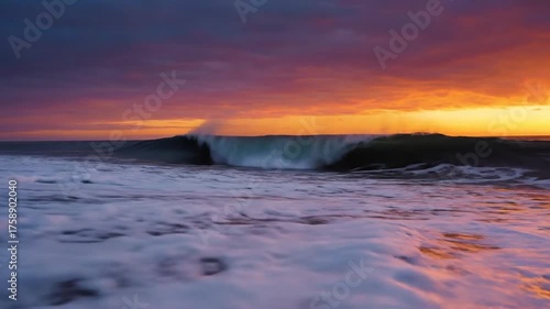 Ocean wave crashing on sandy shore under colorful sunset sky