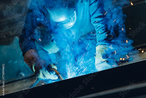 Quadro su tela Skilled worker welding metal at shipyard with blue sparks in industrial setting
