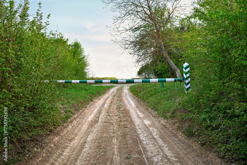 Dirt road leading into a forest blocked by a green and white barrier
