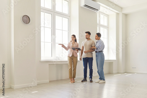 Canvastavla Realtor guides a young couple through a bright empty apartment with large windows and neutral interior