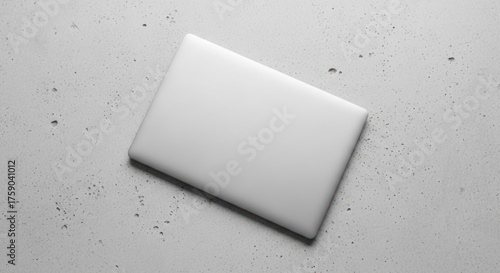 Closed white laptop resting on a textured gray concrete surface.