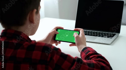 Young man playing mobile game on smartphone with green screen at home.