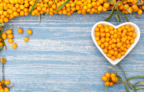 Sea buckthorn berries in a heart-shaped bowl on rustic wooden background – top view