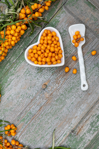 Sea buckthorn berries in a heart-shaped bowl on rustic wooden background – top view