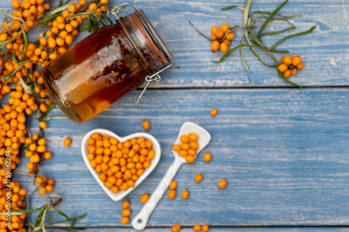 Sea buckthorn berries in a heart-shaped bowl on rustic wooden background – top view