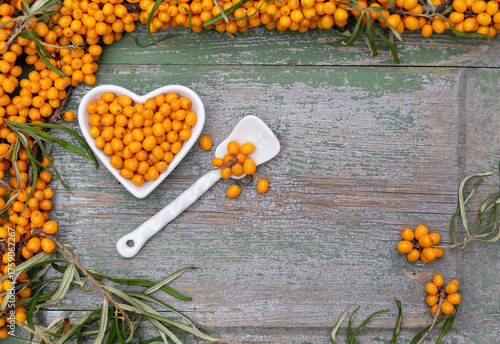 Sea buckthorn berries in a heart-shaped bowl on rustic wooden background – top view