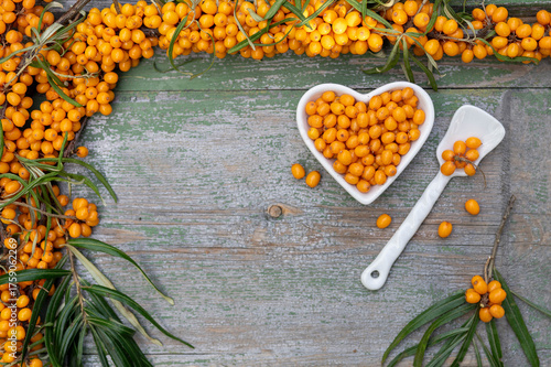 Sea buckthorn berries in a heart-shaped bowl on rustic wooden background – top view