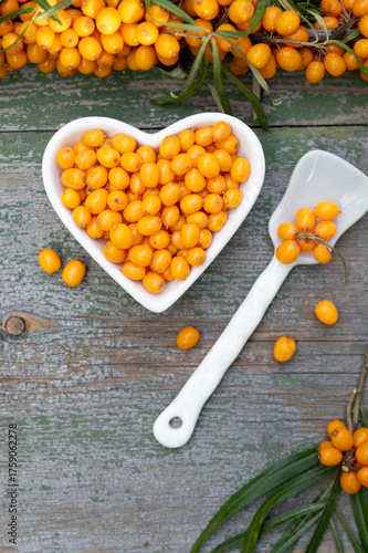 Sea buckthorn berries in a heart-shaped bowl on rustic wooden background – top view