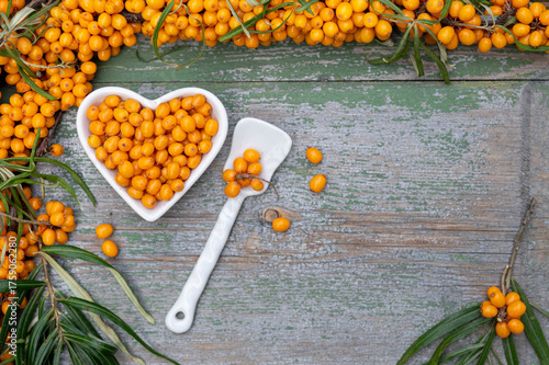 Sea buckthorn berries in a heart-shaped bowl on rustic wooden background – top view