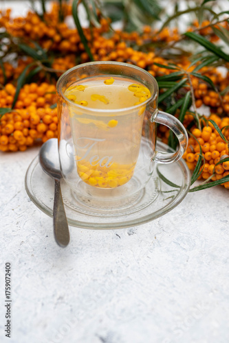 Sea buckthorn tea in a glass cup surrounded by fresh berries – healthy herbal drink